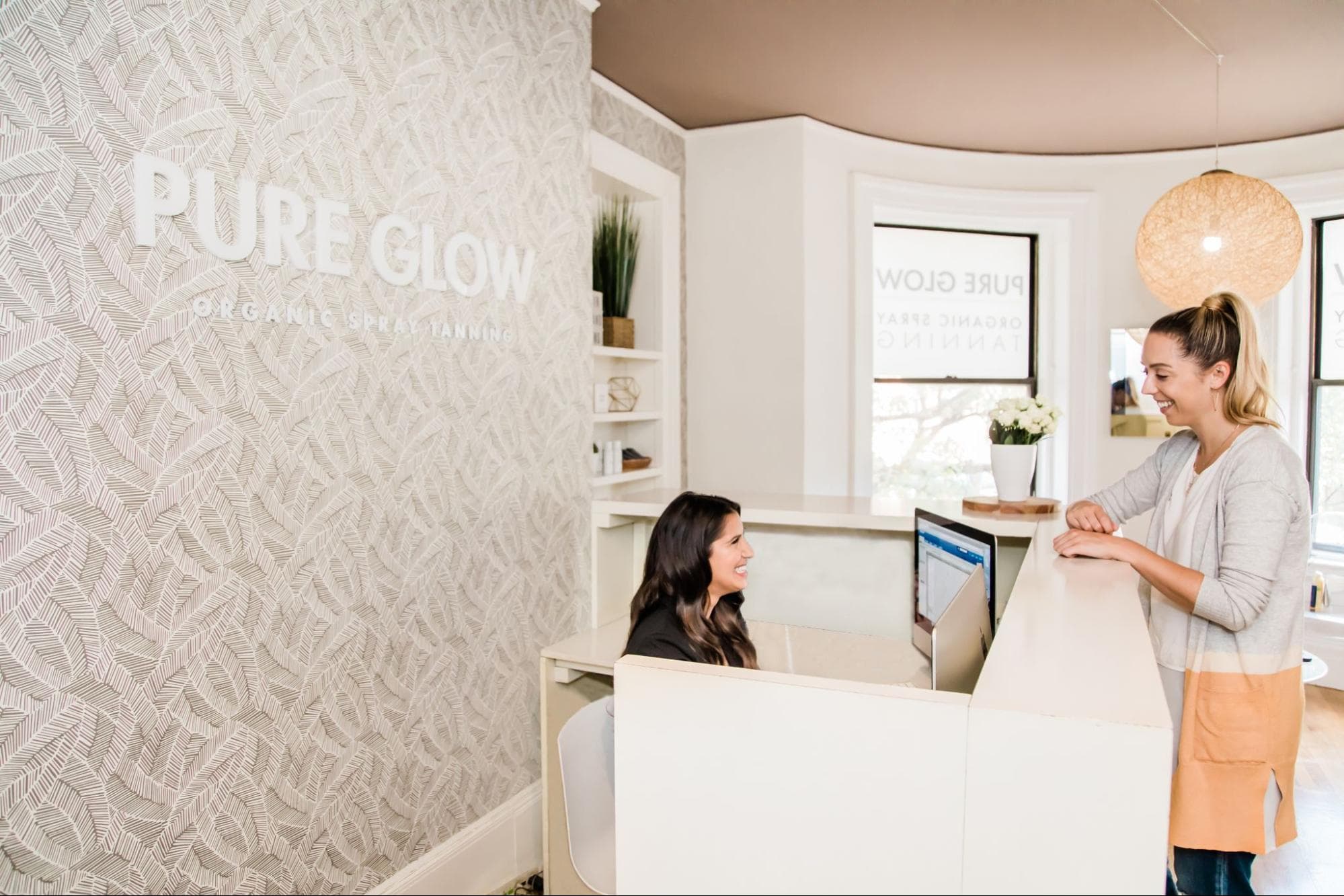 A smiling client is greeted by a cheerful receptionist at Pure Glow.