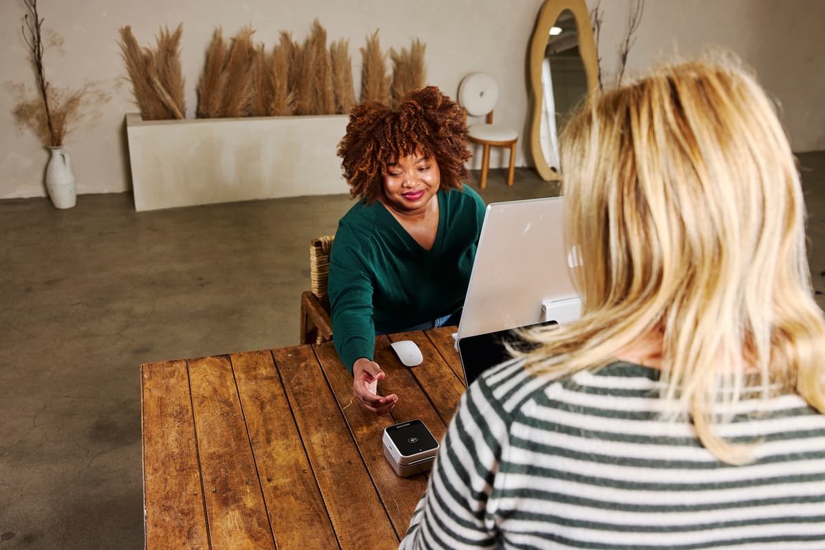 A client uses a Buy Now, Pay Later payment option on a card reader at a salon front desk while a staff member assists.